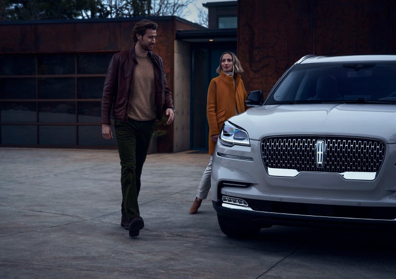 A man and a woman approaching a 2024 Lincoln Aviator® SUV, which illuminates certain lights when they are close | Carman Lincoln in New Castle DE