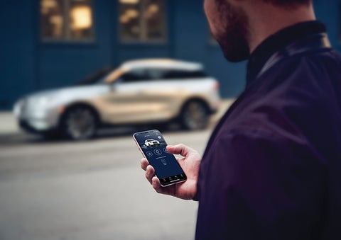 A person is shown interacting with a smartphone to connect to a Lincoln vehicle across the street. | Carman Lincoln in New Castle DE