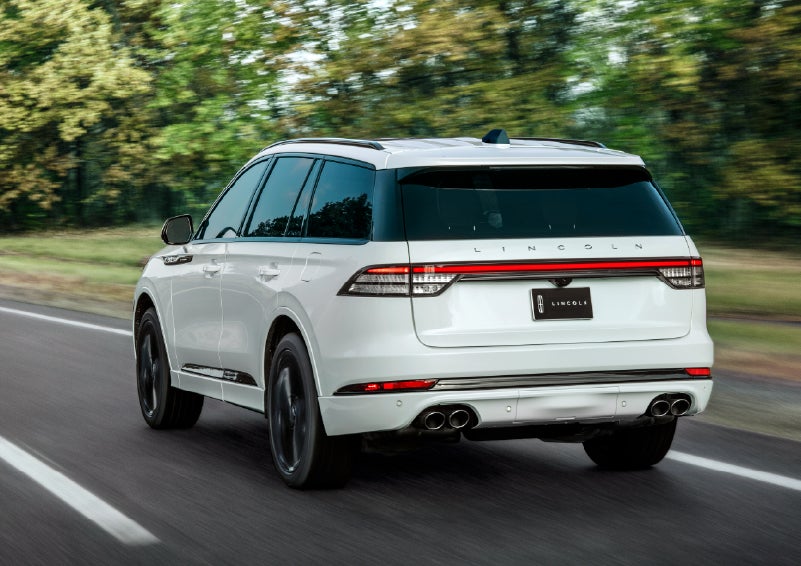 A white 2026 Lincoln Aviator® SUV is being driven away down a road lined with colorful trees. | Carman Lincoln in New Castle DE