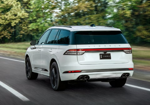 A white 2026 Lincoln Aviator® SUV is being driven away down a road lined with colorful trees. | Carman Lincoln in New Castle DE