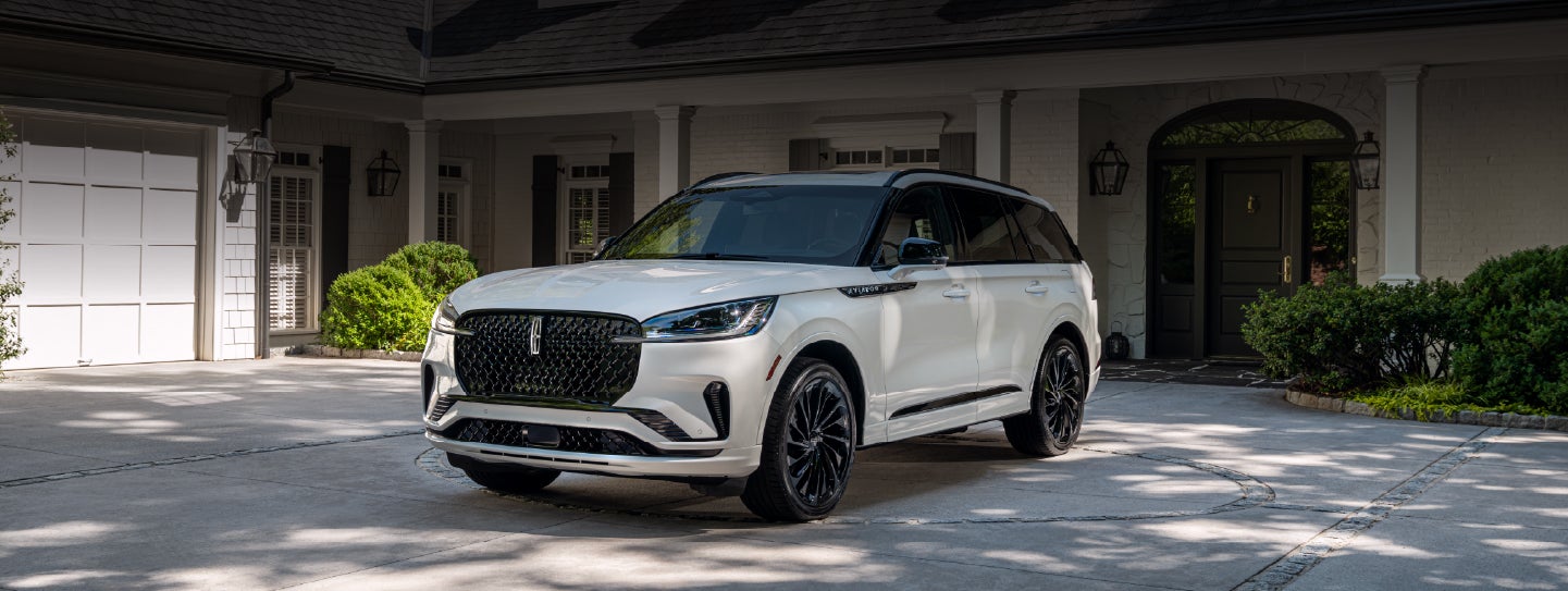 A white 2026 Lincoln Aviator® SUV is parked in the driveway of a luxury home. | Carman Lincoln in New Castle DE