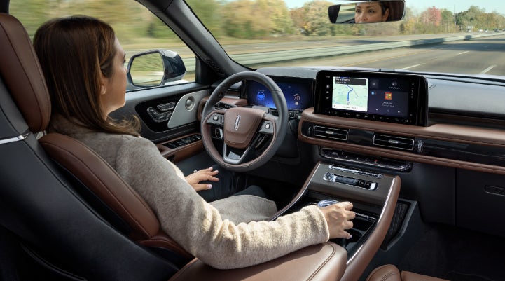 A 2027 Lincoln Aviator® SUV is being driven hands-free on a highway lined with trees. | Carman Lincoln in New Castle DE