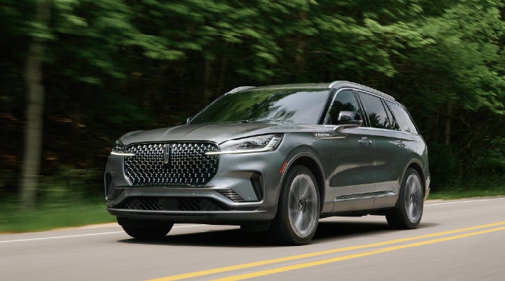 A 2027 Lincoln Aviator® SUV is being driven down a road lined with trees. | Carman Lincoln in New Castle DE